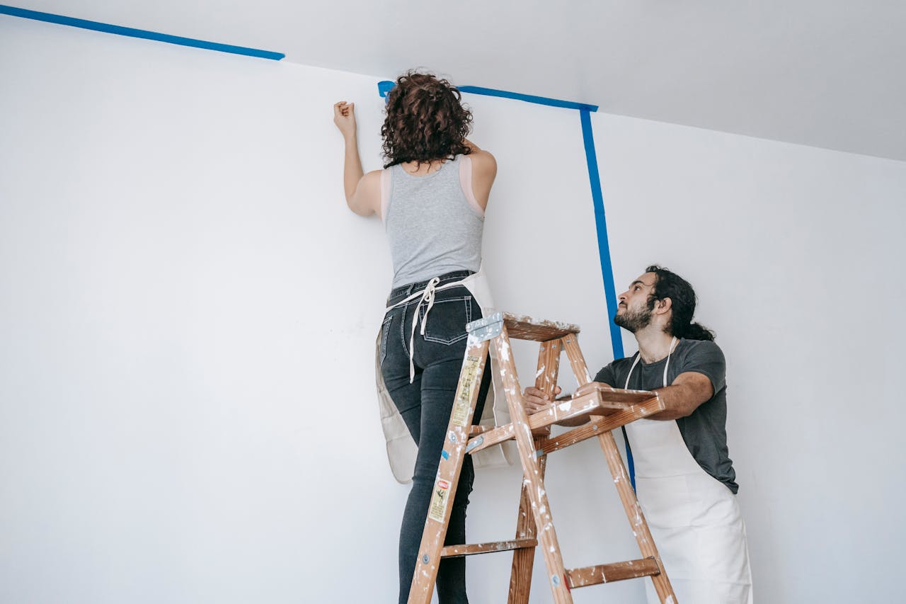 person on ladder putting up tape on a wall. Image by Pexels